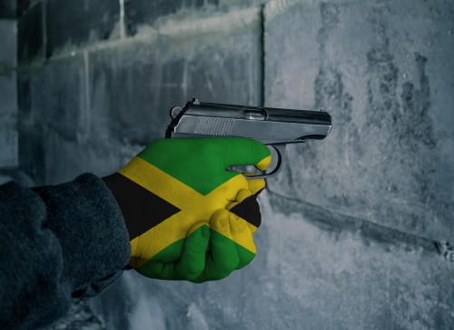 The flag of Jamaica is on the hand holding the gun. Military concept.