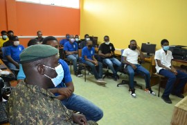 Private Damien Barrow of The Barbados Defence Force (right in military attire) and several IGT ASA beneficiaries tune in to presenters on a screen ahead during an all-male virtual empowerment session hosted by IGT. Barrow had earlier addressed young male participants joining the session from Antigua, Barbados, Jamaica, St. Kitts & Nevis and Trinidad & Tobago.