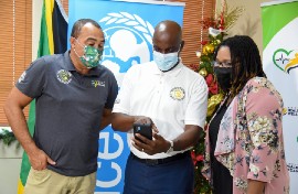 Health and Wellness Minister, Dr. Christopher Tufton (left), and Monitoring and Evaluation Specialist, United Nations Children’s Fund (UNICEF), Donneth Edmondson (right), are given a demonstration of the digitization of Jamaica’s COVID-19 vaccination card system (JIS photo)