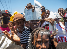 Haitian citizens hold up their passports as they gather in front of the US Embassy in Tabarre, Haiti on July 10, 2021, asking for asylum after the assassination of President Jovenel Moise explaining that there is too much insecurity in the country and that they fear for their lives. (Photo by Valerie Baeriswyl / AFP) (Photo by VALERIE BAERISWYL/AFP via Getty Images)