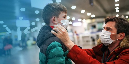 father putting medical mask on his son to protect himself from the coronavirus in an airport terminal or shopping mall