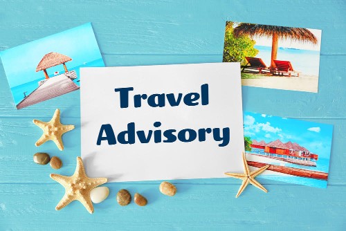 Concept of tourism. Paper with text TRAVEL ADVISORY and photos on wooden background