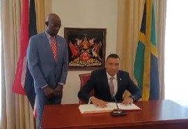 Jamaica Prime Minister Andrew Holness signing visitor’s book watched by his host and fellow Prime Minister Dr. Keith Rowley (Photo Office of the Prime Minister)