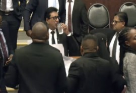 Government legislators surround Attorney General, Anil Nandlall, who is drinking water, as he makes a statement on behalf of President Irfaan Ali as opposition legislators protest.
